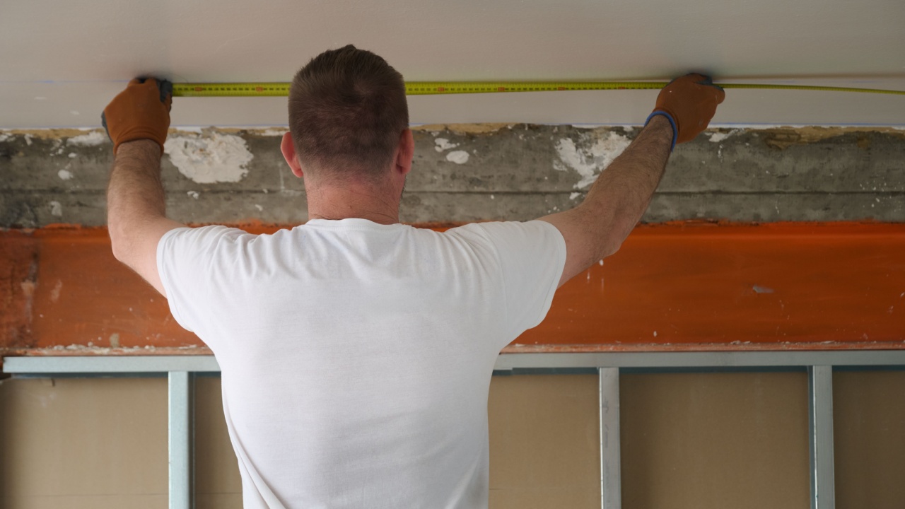 Construction worker wearing gloves accurately measuring a ceiling with a tape measure, preparing for drywall installation