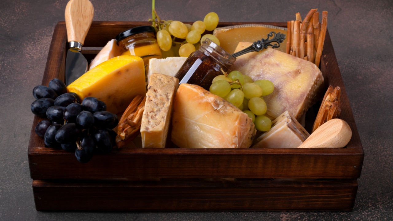 Assorted cheeses, fig jam, honey, grape and knives in a wooden box on a dark background. Gift set idea