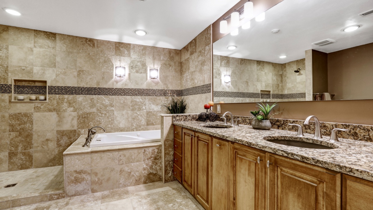Luxury bathroom interior with tile floor. Bath tub with brown granite tile trim and vanity cabinet with large mirror.