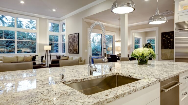 White kitchen design features large bar style kitchen island with granite countertop illuminated by modern pendant lights. Northwest, USA