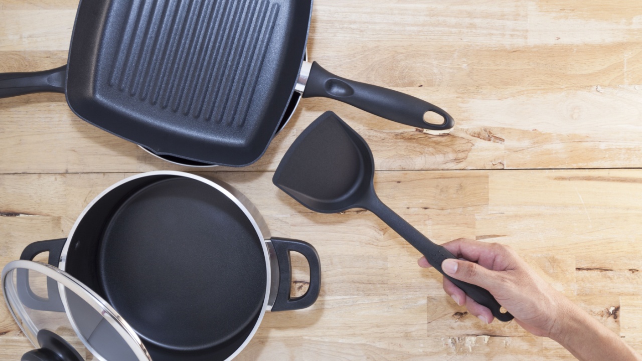 Hand holding plastic spade of frying pan on wood background