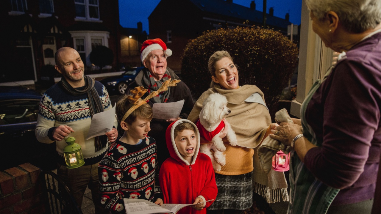 Three generation family are doing door-to-door carol singing. There is a senior woman at the door, appreciating their singing.