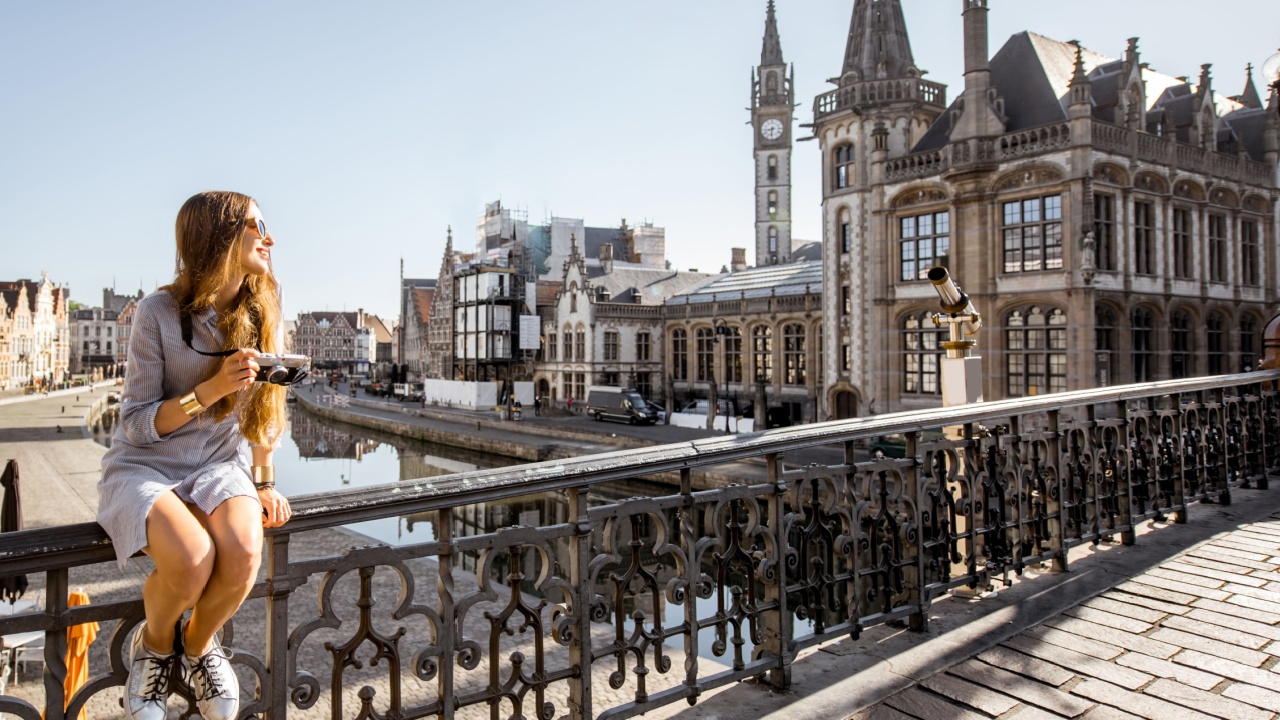 Young woman tourist sitting on the bridge in the old town of Gent city during the sunrise in Belgium