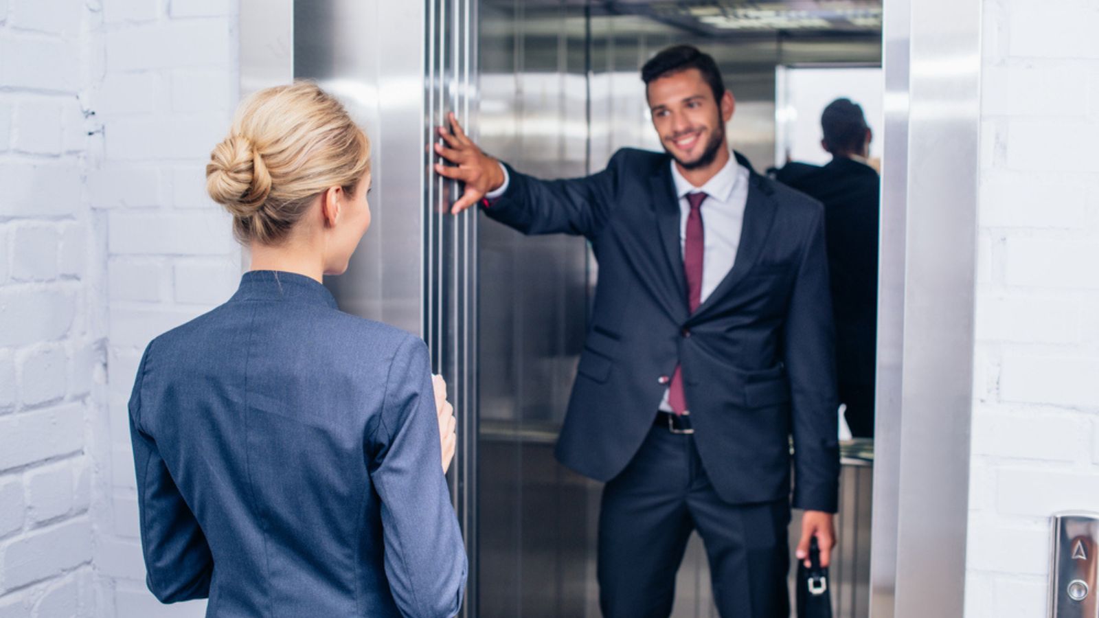 Smiling handsome businessman holding elevator door for woman