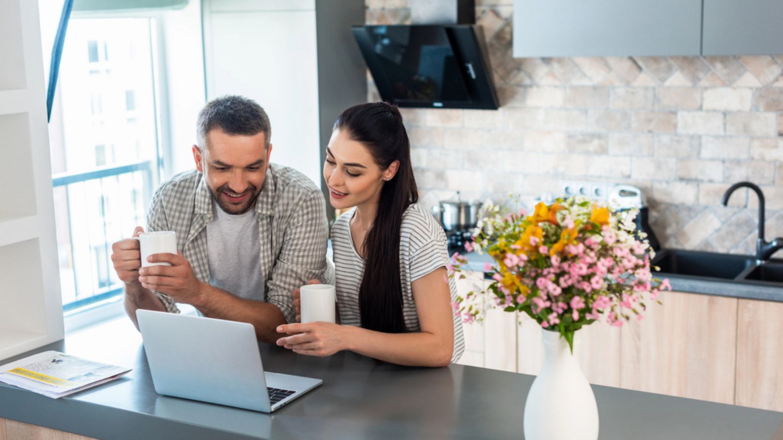 Smiling married couple looking at laptop screen together at counter in kitchen