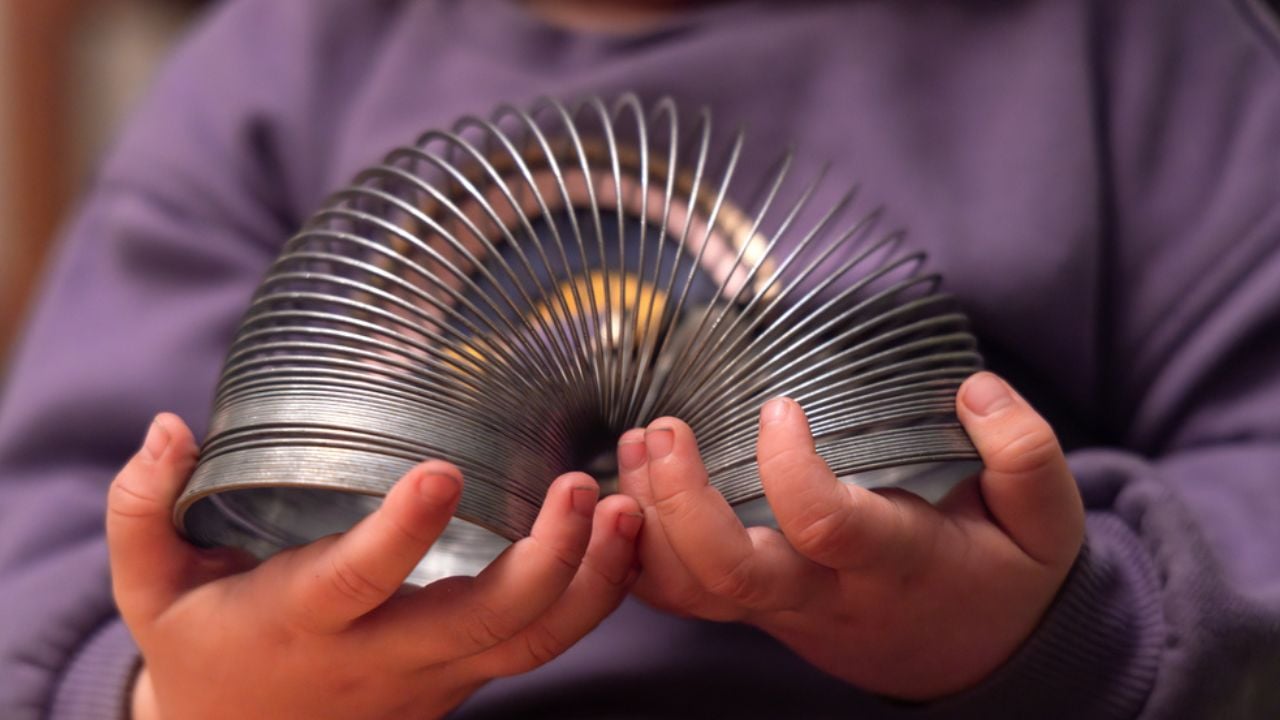 Toddlers hands gently manipulating a flexible metal spring toy, showcasing the principles of elasticity and childhood amusement