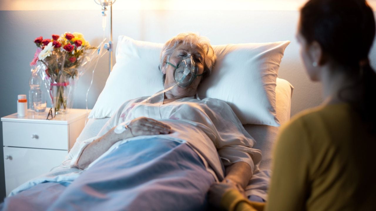 Woman assisting and supporting her senior mother lying in bed at the hospital, she is holding her hand