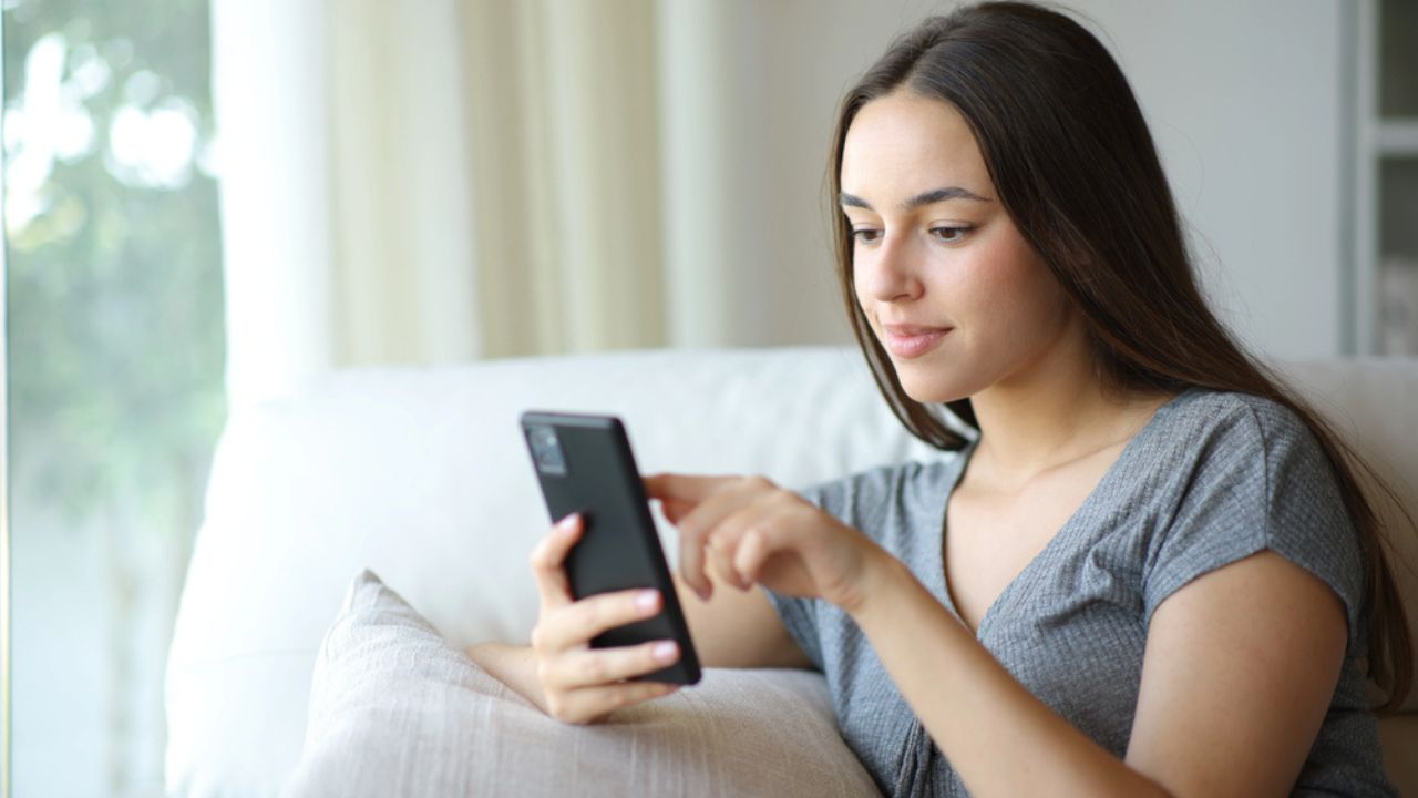 Woman checking online content on mobile phone sitting on a couch at home
