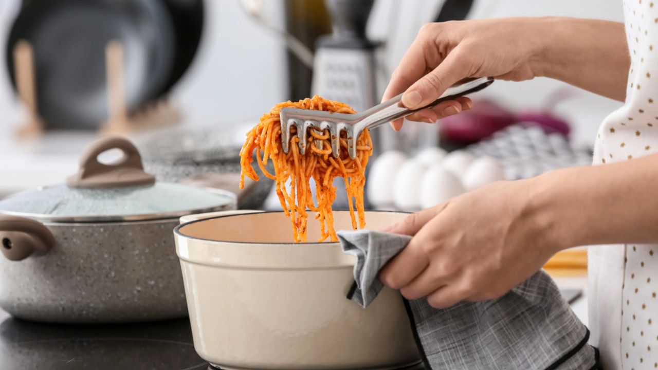 Woman cooking tasty pasta in kitchen
