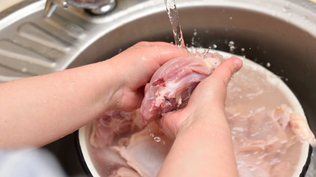 Woman washes the chicken meat in the sink