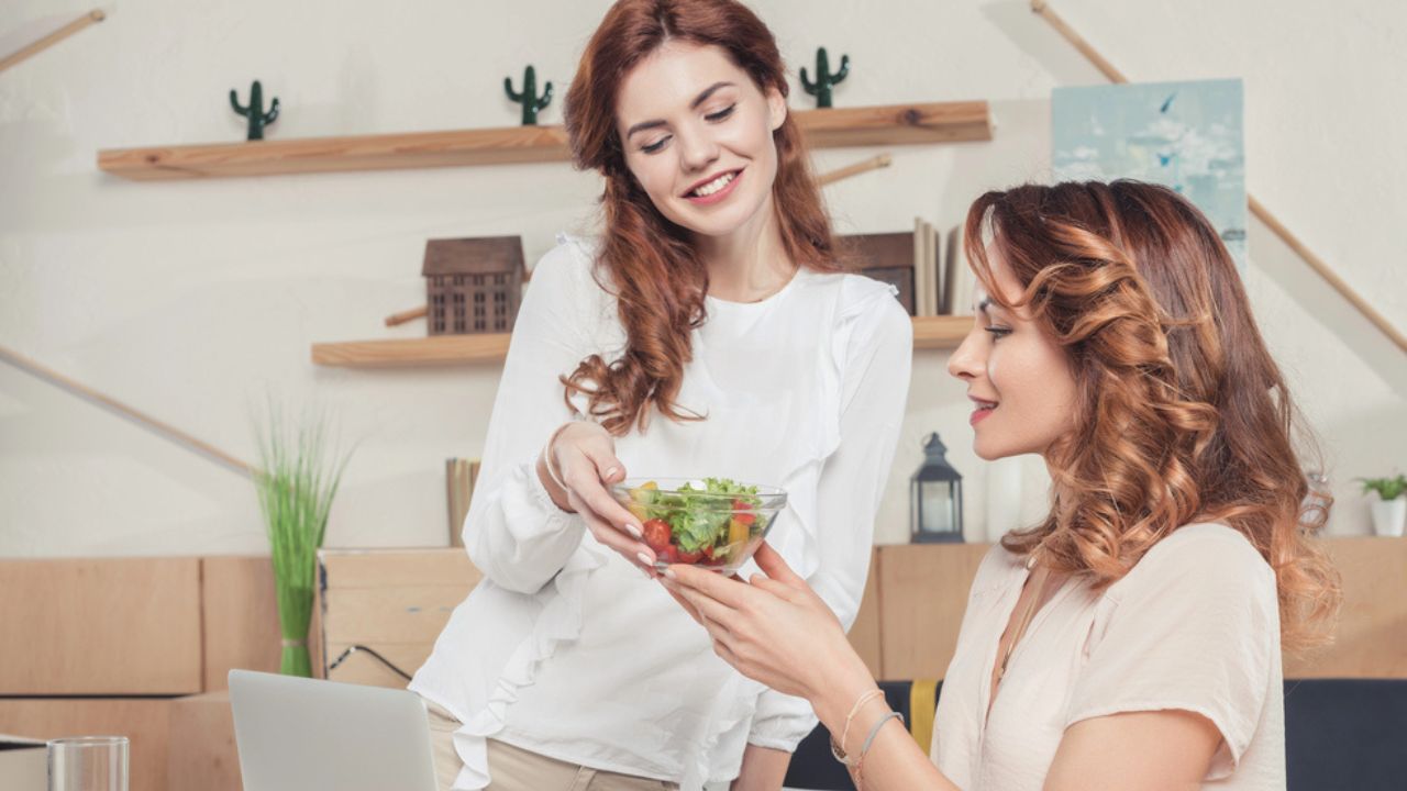 Young businesswoman giving healthy salad to colleague