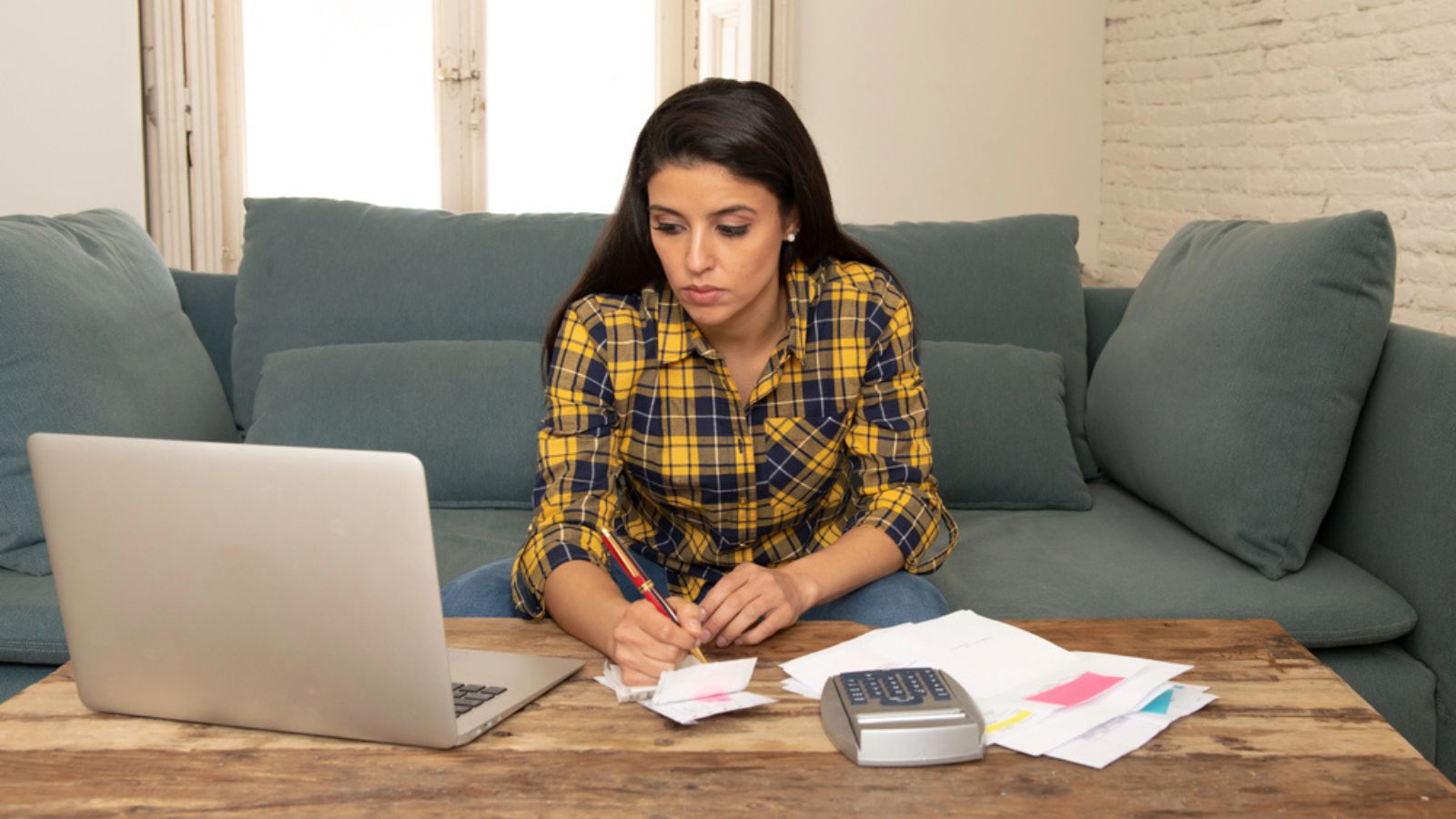 Young worried woman in stress banking and accounting debt bills, bank papers, expenses and payments with computer at home feeling desperate in a bad financial situation.