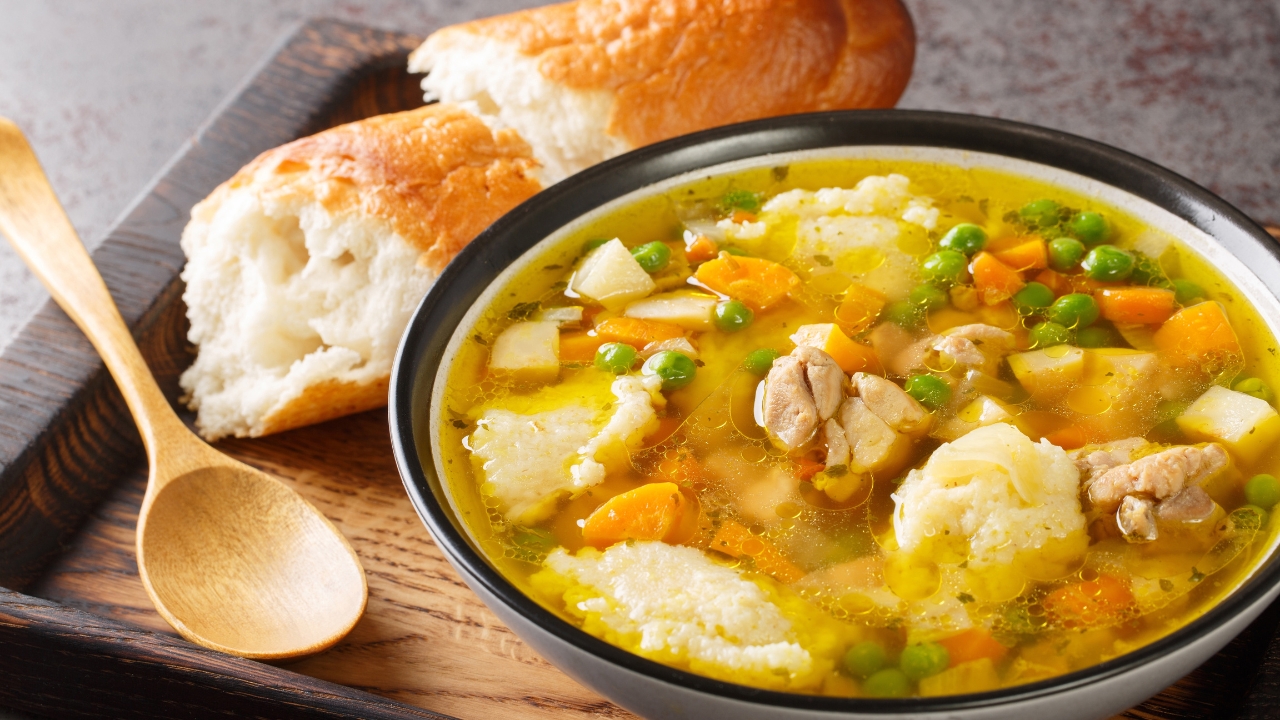 a bowl of chicken and dumplings with two rolls