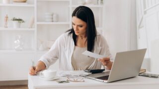 focused woman doing taxes bills on laptop and drinking coffee