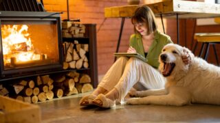 a young woman pats her dog in front of a woodstove