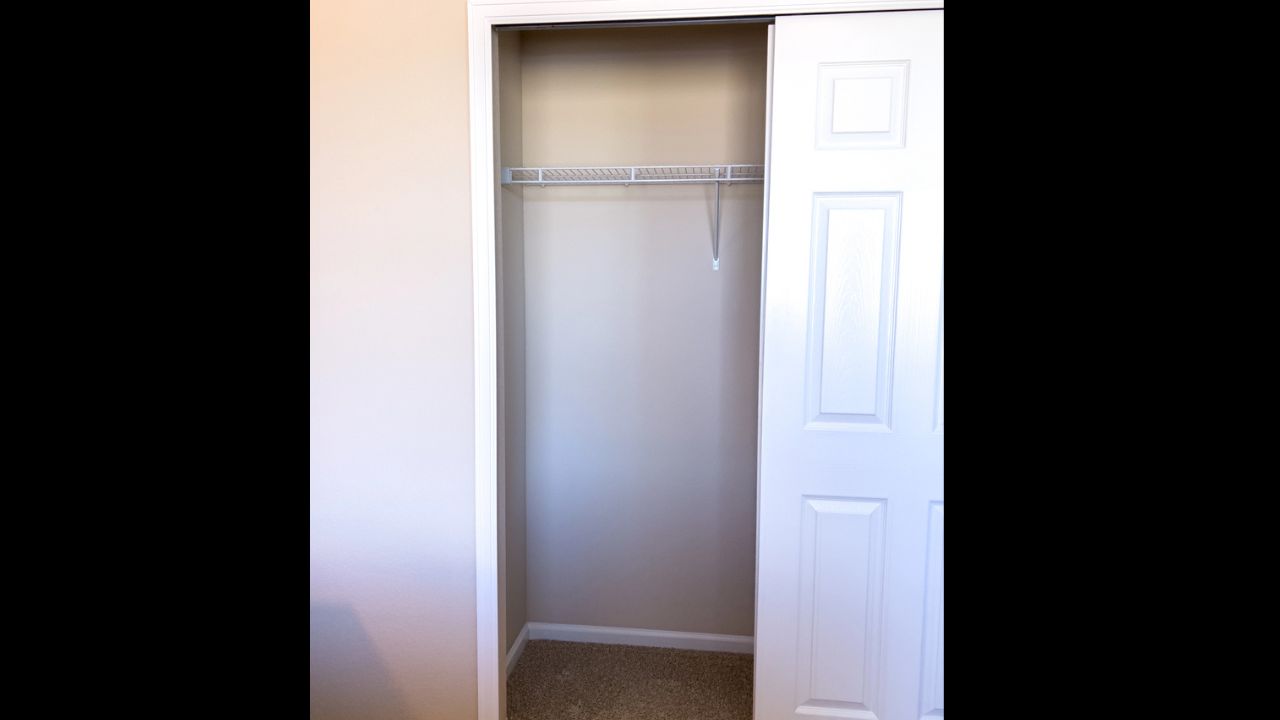 A small bedroom closet with double white doors is shown open