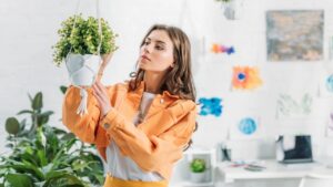 Beautiful woman in orange clothing touching hanging flowerpot at home