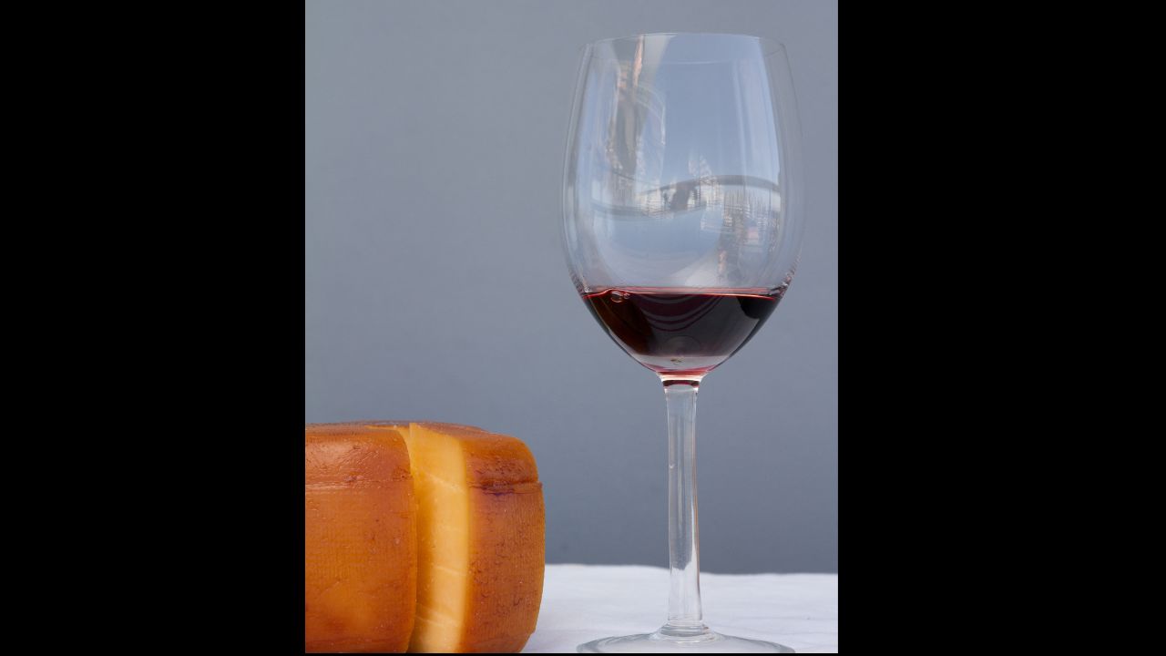 Cheese wheel and glass of Malbec wine over a wooden table.