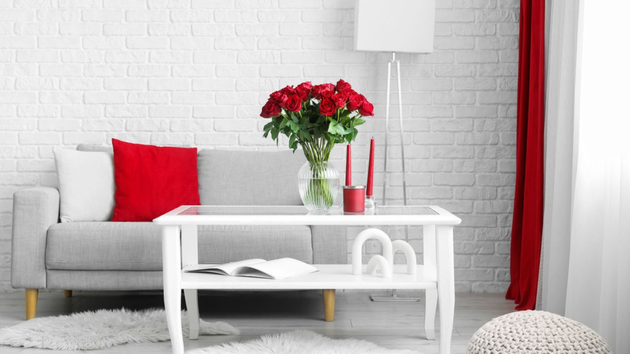 Interior of stylish living room with grey sofa, standard lamp and beautiful red roses on glass coffee table
