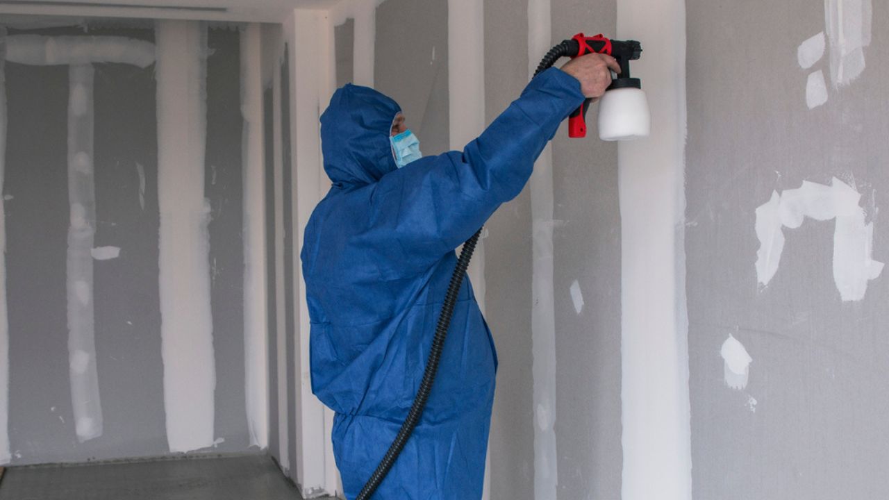 Man in a special suit paints walls with a spray gun, painting walls and ceilings