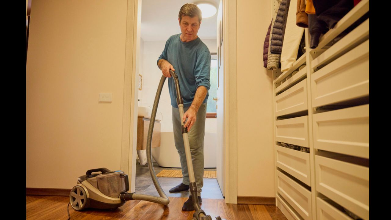 Middle-aged man cleans the house with a vacuum cleaner,