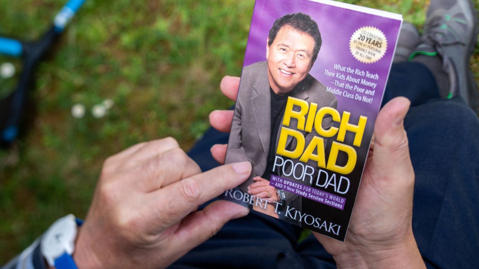 Paris, France - May 3, 2020 Overhead POV view of senior male hand hodling in had reading the iconic book Rich dad and Poor Dad by Robert T Kiyosaki