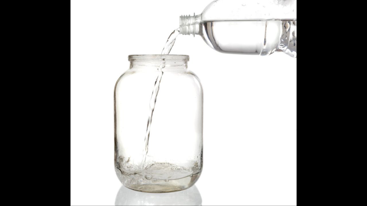 Pouring water into an empty glass jar on a white background