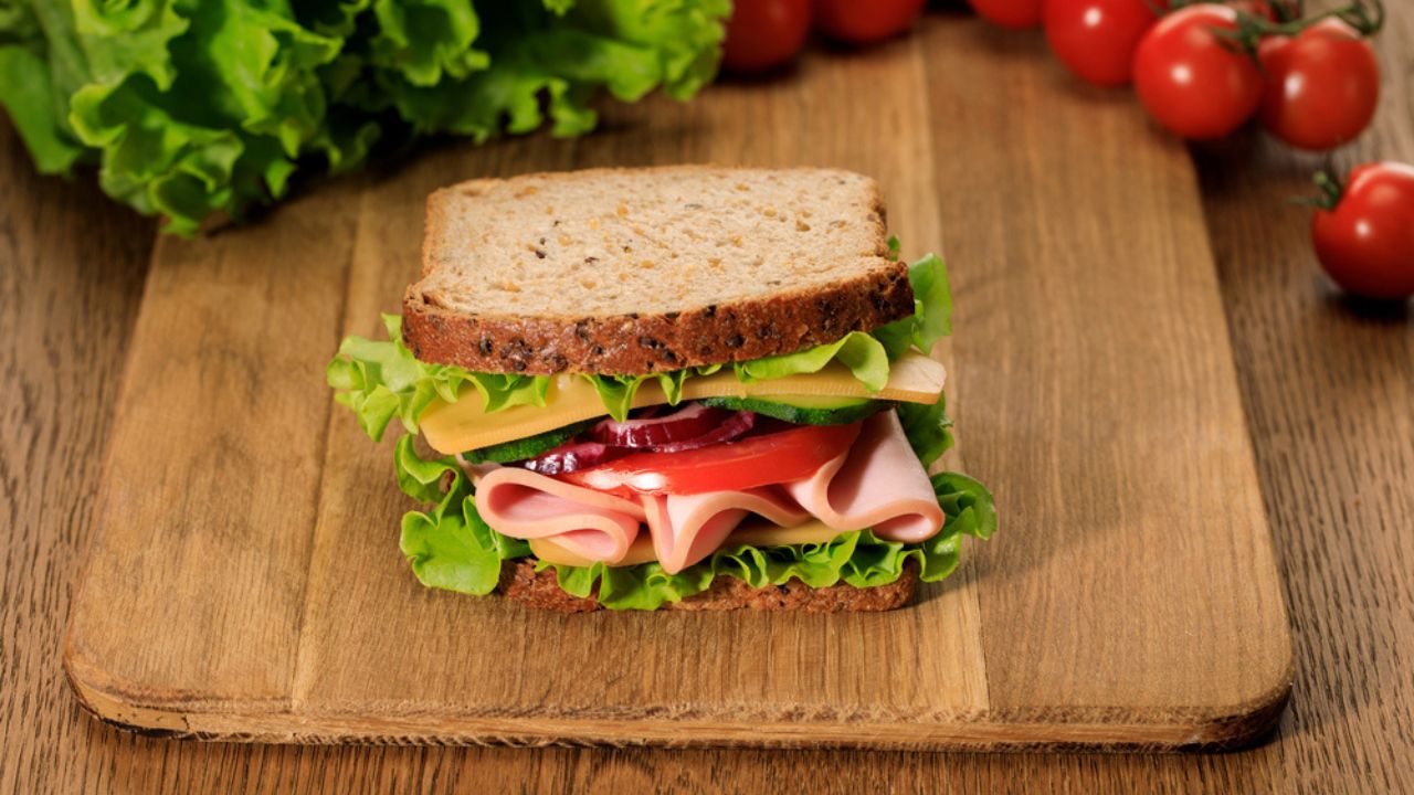 Selective focus of fresh sandwich on wooden cutting board near lettuce and cherry tomatoes