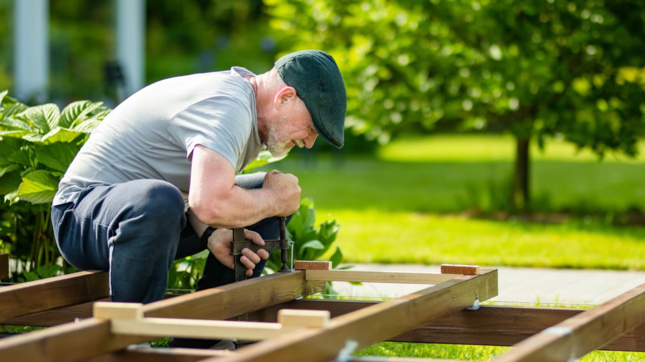 Senior man working on a project in his garden. Man constructing a wooden terrace on his backyard.
