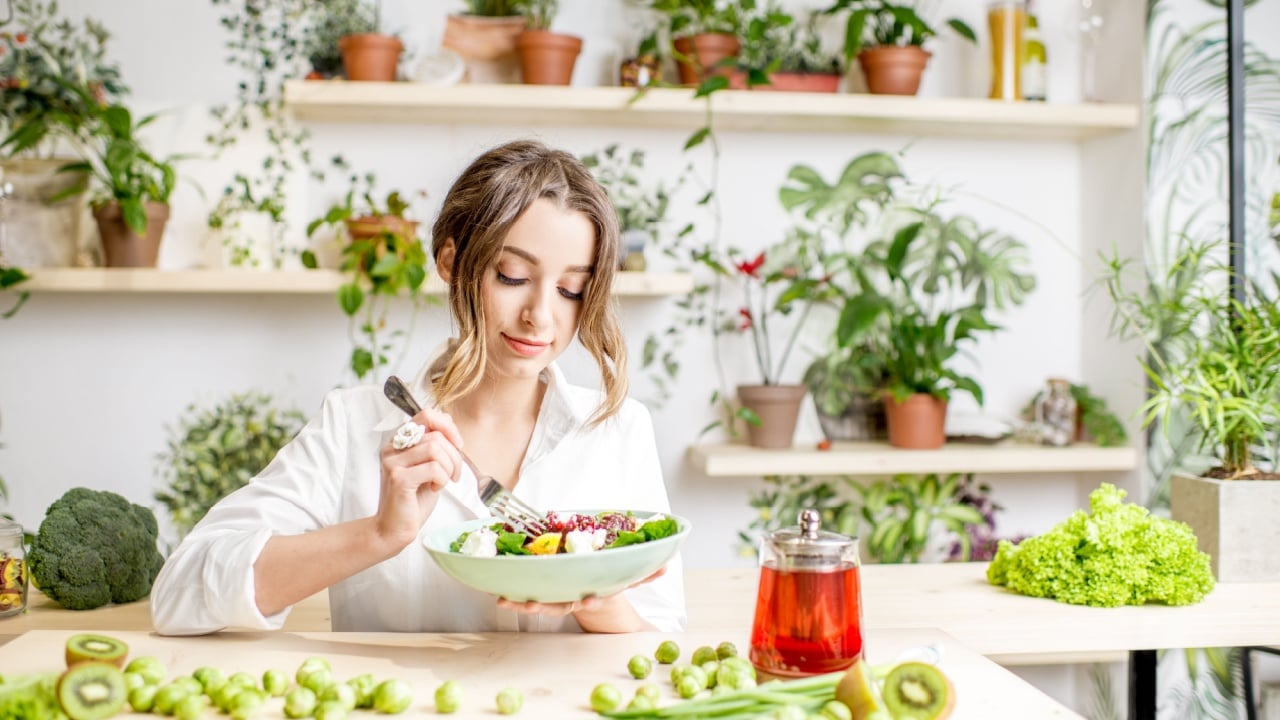 Young woman eating healthy food sitting in the beautiful interior with green flowers on the background