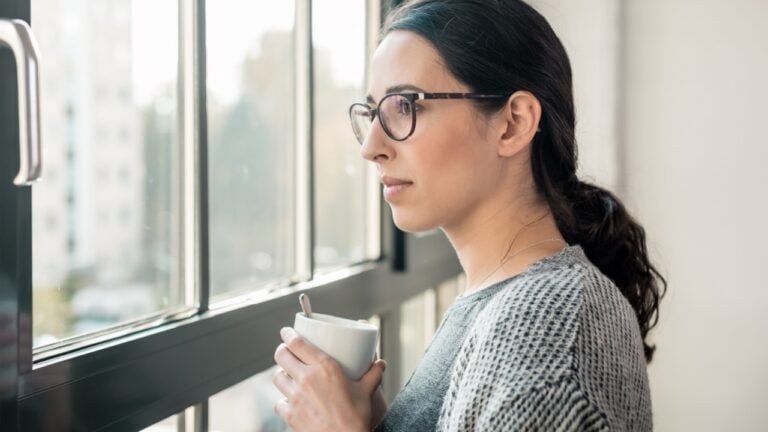 Young pensive woman with serious facial expression looking through the window during break at work