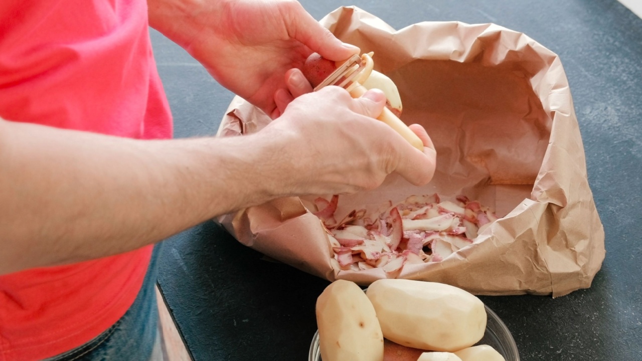 Man's hands peeling potatoes. Paper bag with cleaning of the potatoes. Potatoes in bowl. Top view.