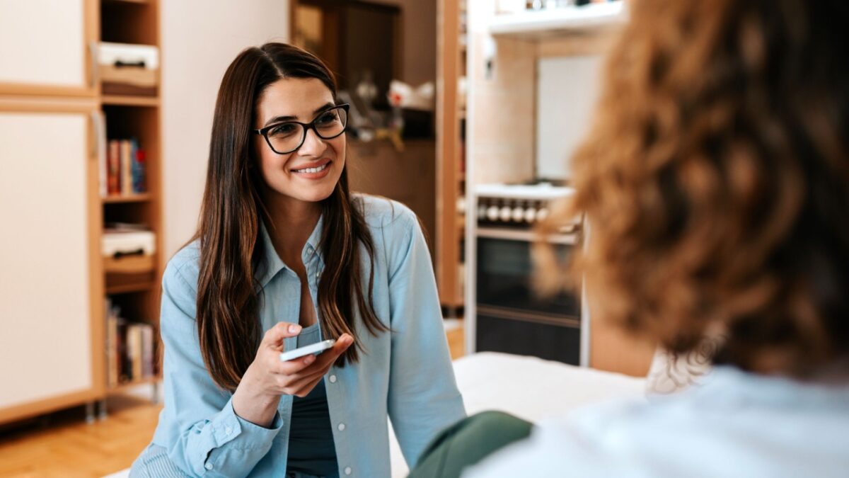 Two young female friends sitting on sofa in the living room at home.