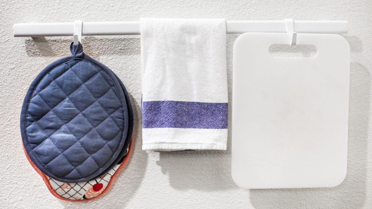 Pot holders, dish towel and cutting board hanging on a rail against white wall