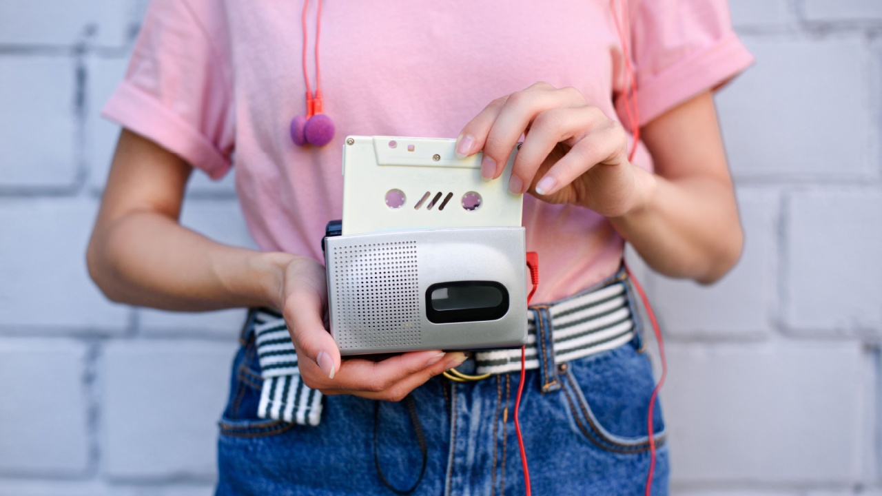 cropped shot of woman with earphones holding retro cassette player and audio cassette in hands mixtapes against white brick wall