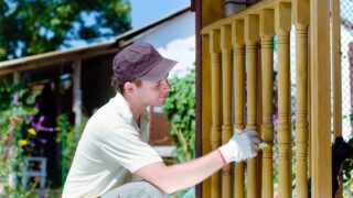 Young man painting wooden fence in the garden