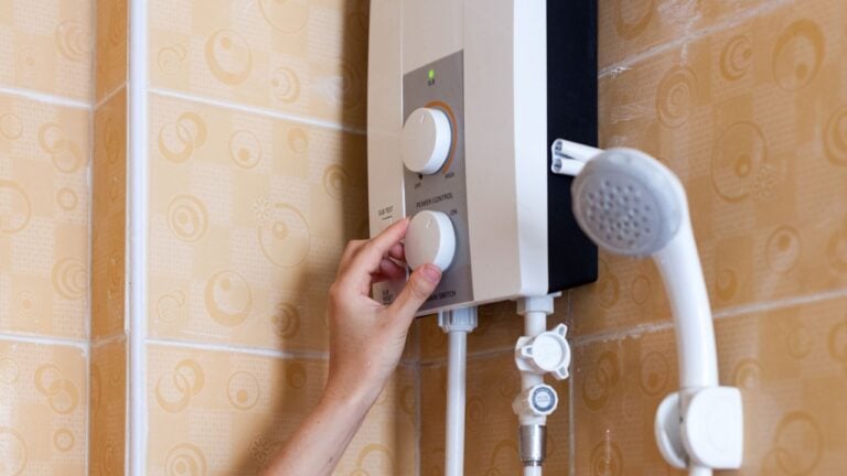 Close-up of hands setting the temperature of water in electric boiler in the shower room