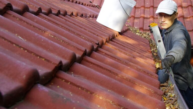 The man on ladder cleans the gutters on the roof. Spring and autumn problem with leaves in gutter.