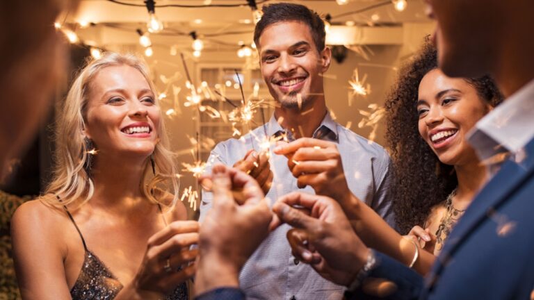 Group of multiethnic friends having fun with sparkling sticks during night party. Group of elegant women and men holding sparklers and celebrating the new year’s eve.