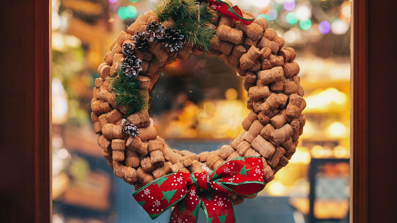 Creative christmas wreath of wine corks, pine cones and red bow on door or window in european city street. Stylish christmas street decor, Festive decorations and illumination. Winter holidays