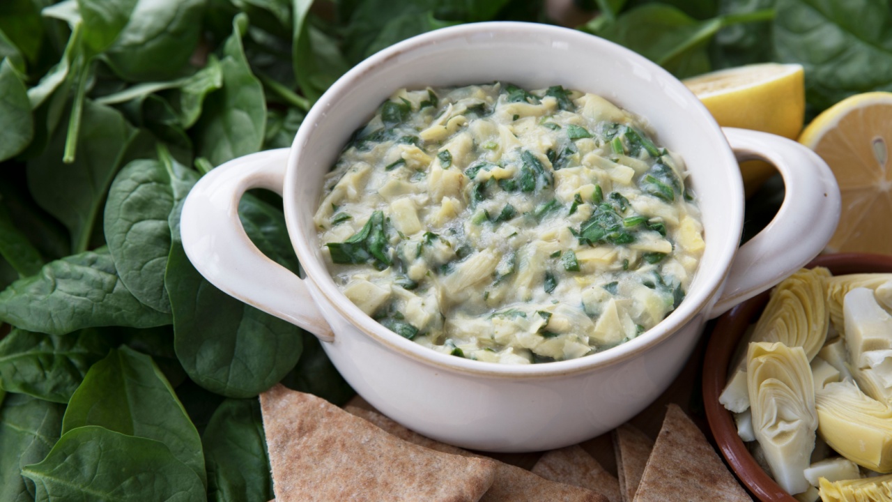 Bowl of vegan spinach artichoke dip with pita and ingredients.