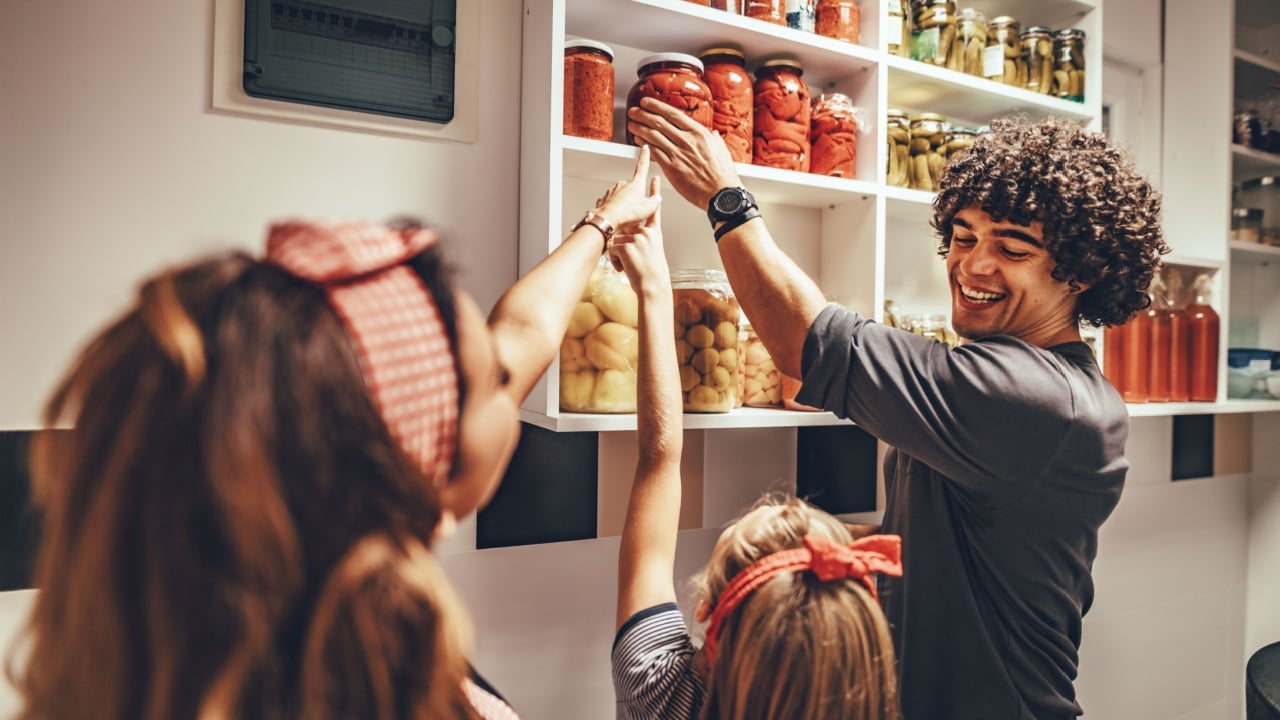 A happy family takes jars with pickled vegetables from the pantry shelf.