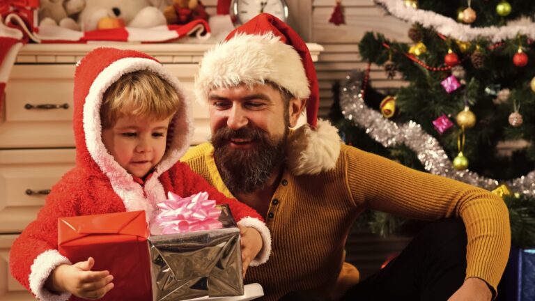 Happy family celebrate new year and Christmas. Father and child with new year present box. Winter holiday and boxing day. Father and son in santa hat at Christmas tree. Xmas party celebration.