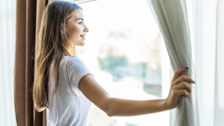girl opening curtains in a bedroom