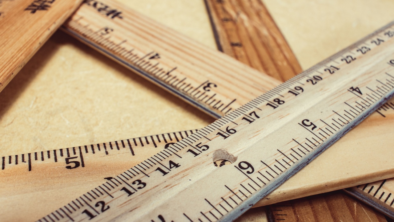 stack of wooden rulers on a tan table, rulers vary in color