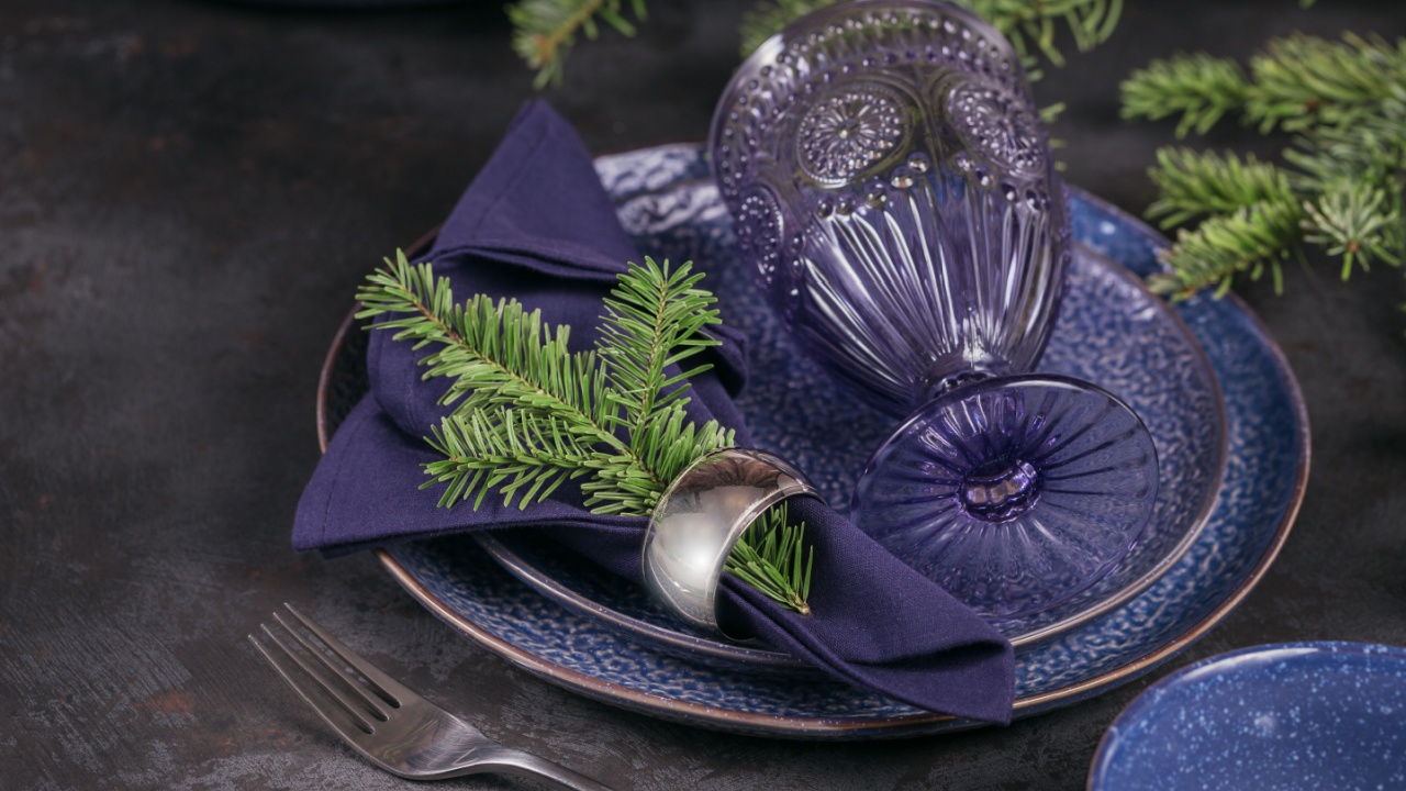 Christmas table setting. Dark blue decoration with fir-tree branch. Plates, wine glasses and cutlery with decorative textile on dark background.