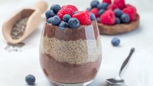 Layered chocolate and peanut butter chia seed pudding in a glass, garnished with raspberry and blueberry