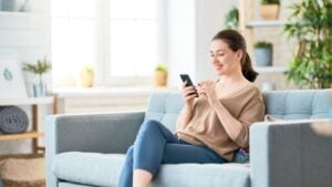 Happy casual beautiful woman is talking on a phone sitting on a sofa at home.