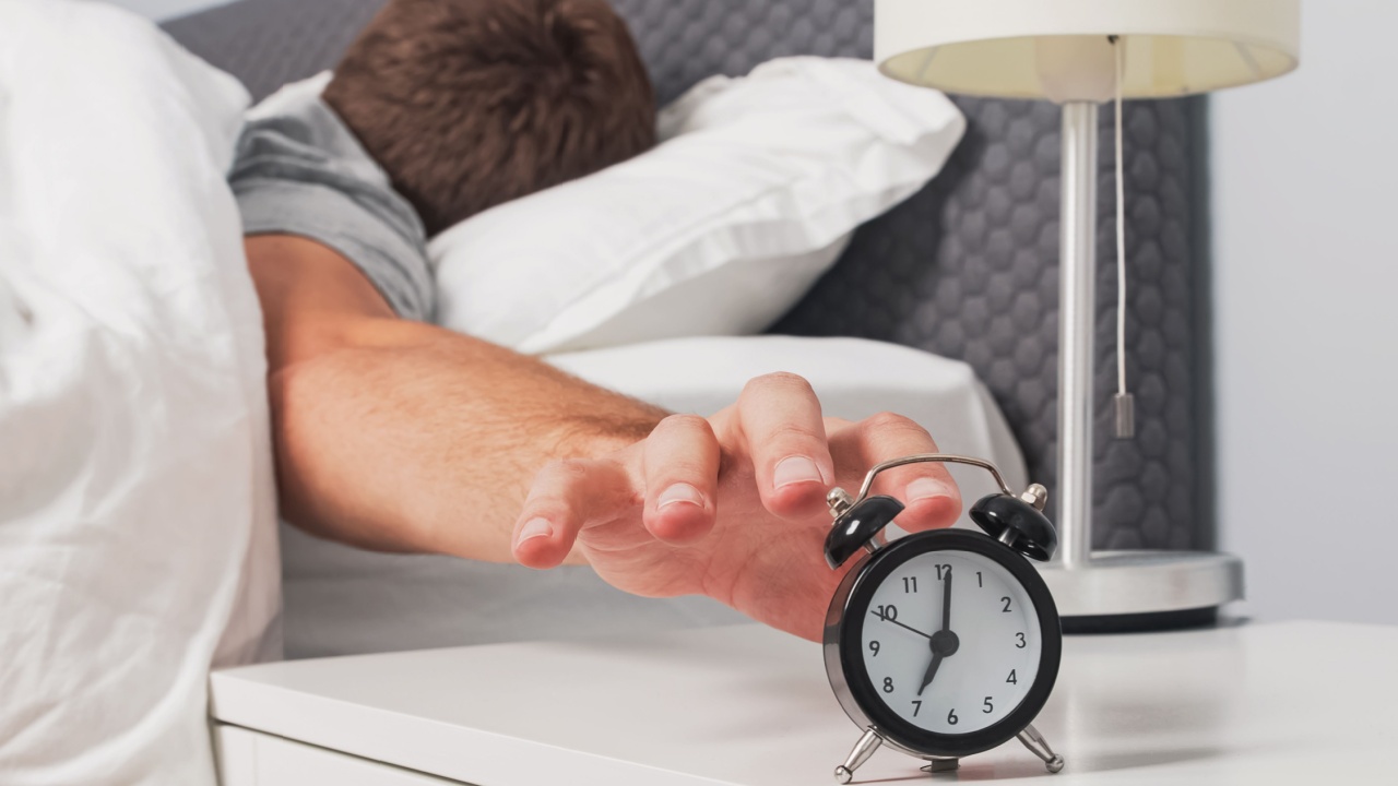 Man's hand reaching out alarm clock on the nightstand early in the morning.