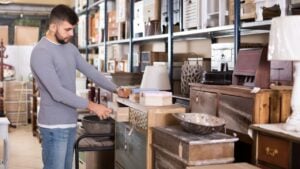 Portrait of handsome male choosing small cabinet in shop of secondhand furniture